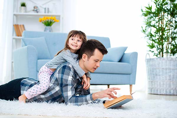 A child sitting on their father’s back reading a book in a cool room